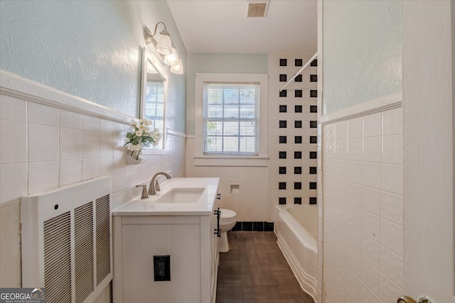 bathroom with toilet, tile patterned floors, tile walls, heating unit, and vanity