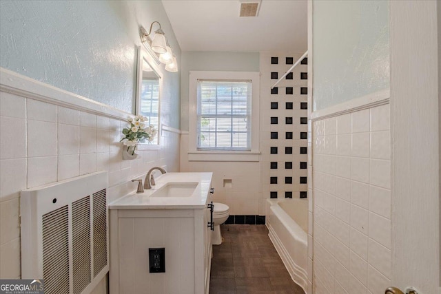 full bathroom with visible vents, tile walls, wainscoting, vanity, and toilet
