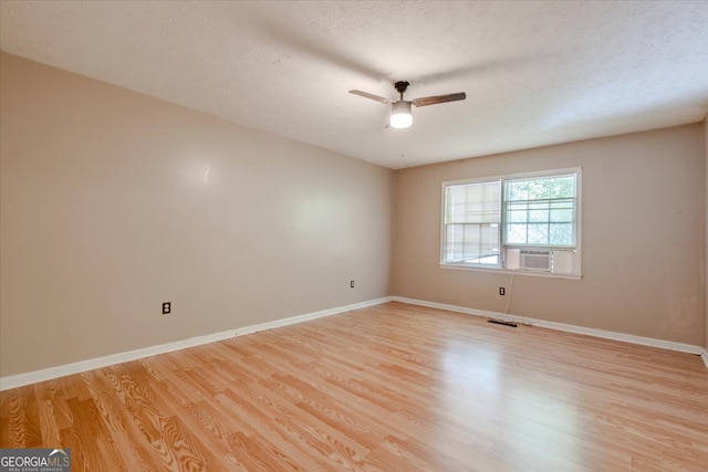 empty room with cooling unit, a textured ceiling, light wood-type flooring, and ceiling fan