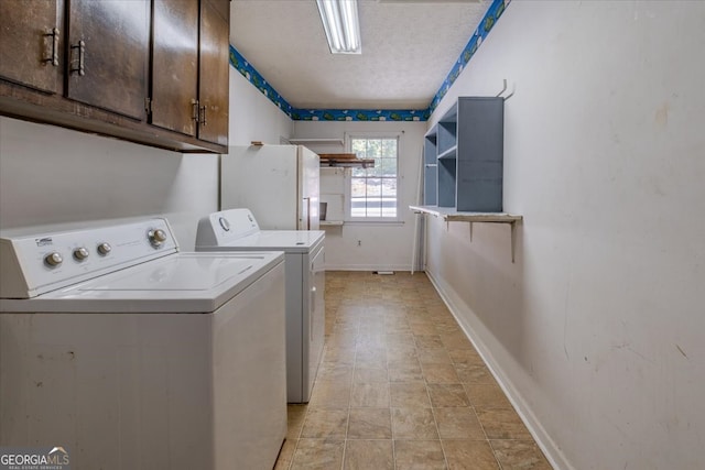 laundry room with a textured ceiling, washing machine and clothes dryer, and cabinets