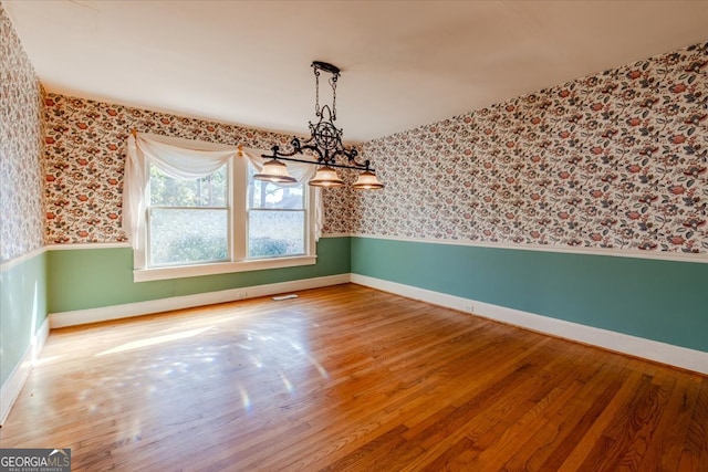 unfurnished dining area featuring an inviting chandelier and wood-type flooring