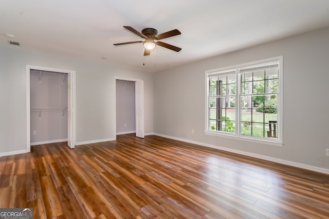 unfurnished bedroom featuring ceiling fan, wood-type flooring, and multiple closets