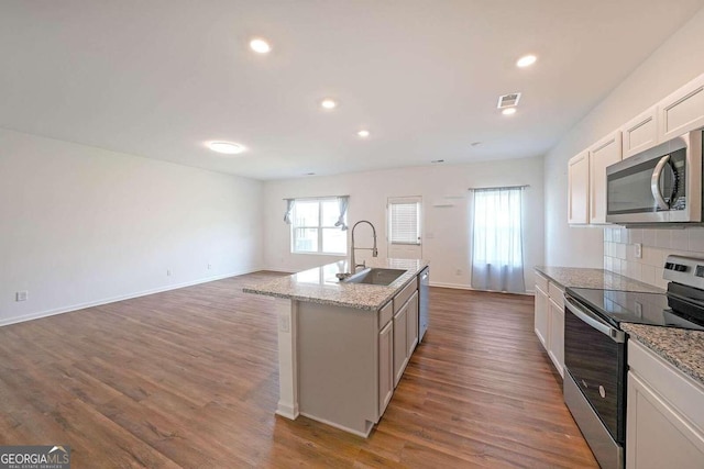 kitchen featuring a sink, appliances with stainless steel finishes, backsplash, dark wood-style floors, and a center island with sink