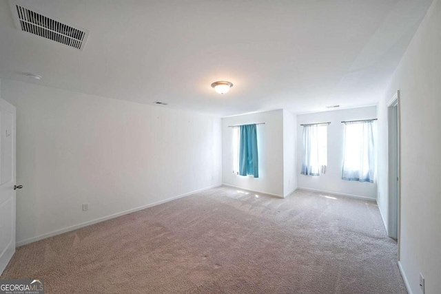 empty room featuring light carpet, visible vents, and baseboards