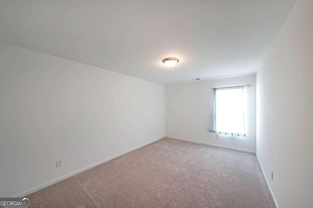 spare room featuring light carpet and baseboards