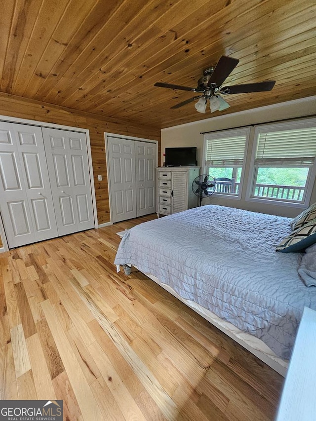 bedroom with two closets, wood walls, ceiling fan, wooden ceiling, and wood-type flooring