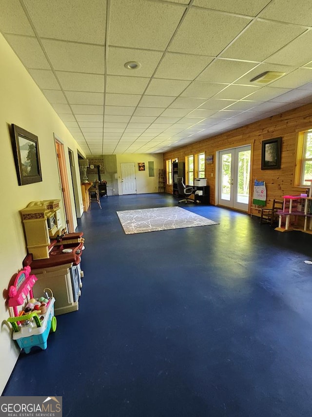 recreation room featuring french doors, a drop ceiling, and wooden walls