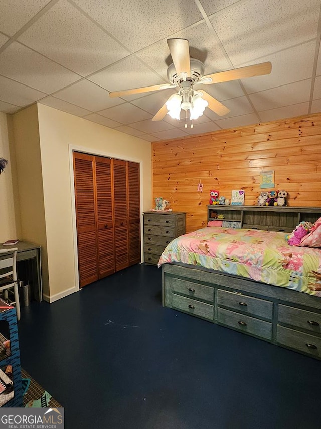 bedroom featuring ceiling fan, a closet, a paneled ceiling, and wood walls