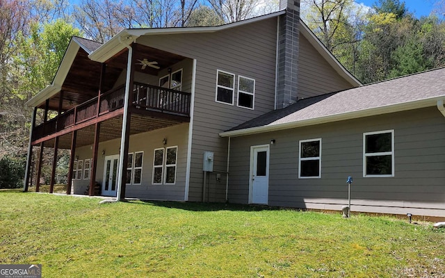 rear view of property featuring ceiling fan, a balcony, and a lawn