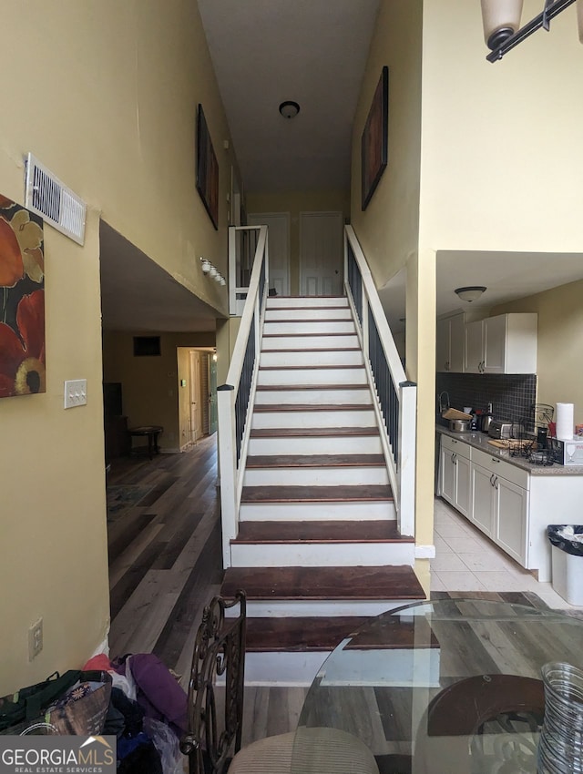 stairs featuring visible vents, a high ceiling, and wood finished floors