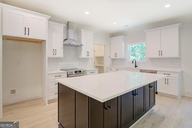 kitchen featuring stainless steel appliances, decorative backsplash, a kitchen island, light hardwood / wood-style floors, and wall chimney exhaust hood