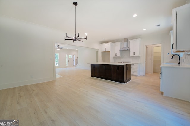 kitchen with white cabinetry, light wood-type flooring, a center island, and wall chimney exhaust hood