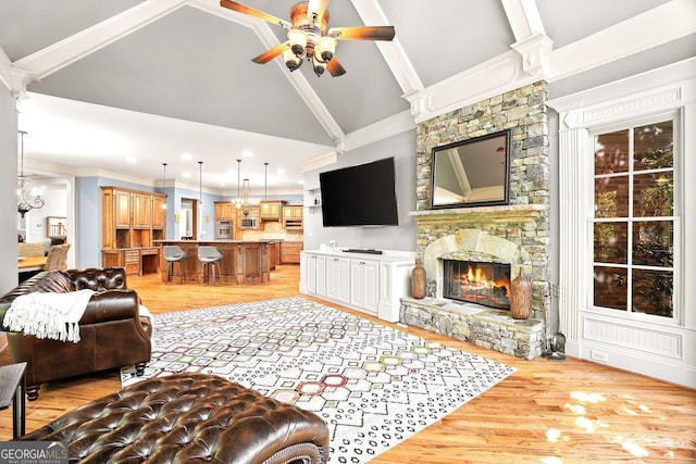 living room with ornamental molding, ceiling fan, high vaulted ceiling, a stone fireplace, and light wood-type flooring