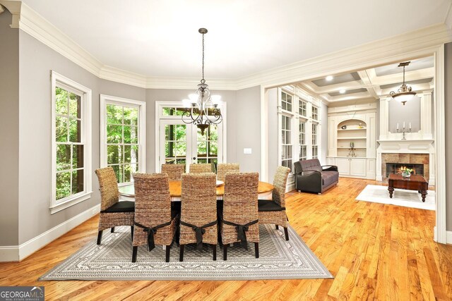 dining area with ornamental molding, a chandelier, light hardwood / wood-style flooring, coffered ceiling, and a tile fireplace