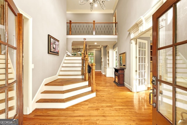 entrance foyer featuring a high ceiling, light wood-type flooring, crown molding, and a notable chandelier