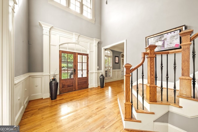 foyer featuring ornate columns, french doors, light hardwood / wood-style flooring, and a high ceiling