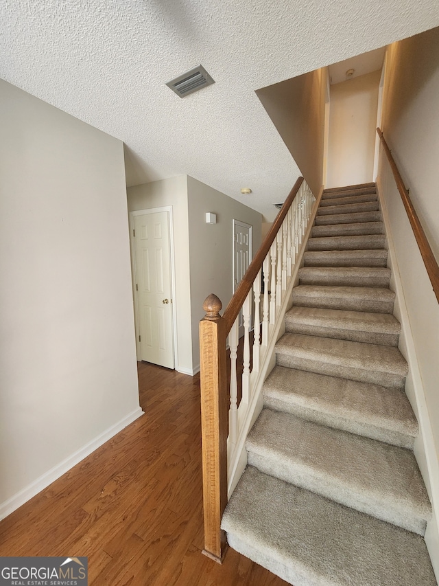 staircase featuring a textured ceiling and hardwood / wood-style floors