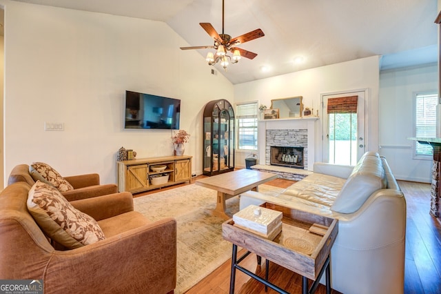 living room featuring ceiling fan, high vaulted ceiling, hardwood / wood-style flooring, and a stone fireplace