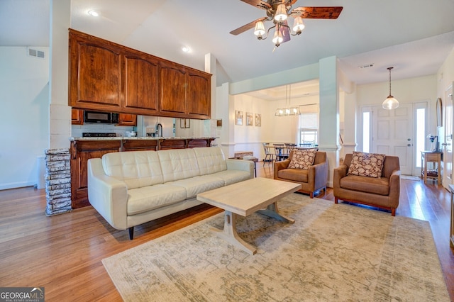 living room with light wood-type flooring, lofted ceiling, ornate columns, ceiling fan, and sink