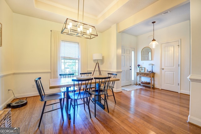 dining area with a chandelier, wood-type flooring, and a raised ceiling