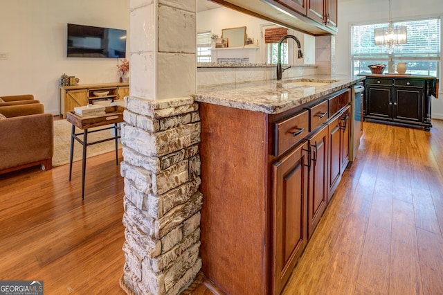 kitchen with light wood-type flooring, sink, light stone counters, and decorative light fixtures