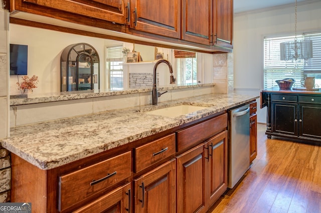 kitchen with light hardwood / wood-style flooring, light stone counters, pendant lighting, stainless steel dishwasher, and sink