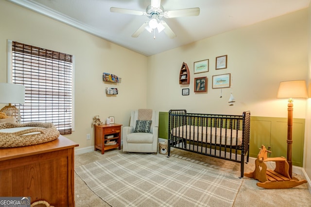 bedroom featuring ceiling fan, a nursery area, and light carpet