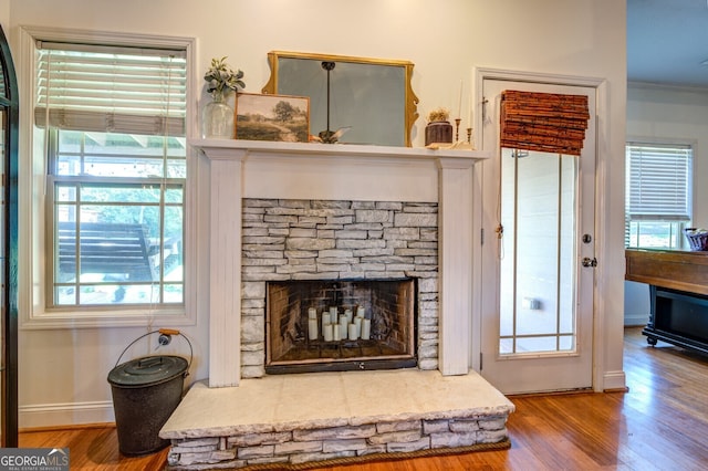 room details featuring wood-type flooring, a stone fireplace, and crown molding