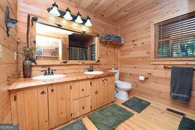 bathroom featuring toilet, wooden walls, dual vanity, wood-type flooring, and wood ceiling