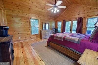 bedroom with ceiling fan, light wood-type flooring, vaulted ceiling, and wooden walls