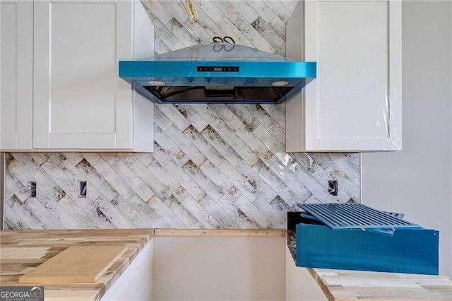 details with tasteful backsplash, white cabinetry, butcher block counters, and exhaust hood