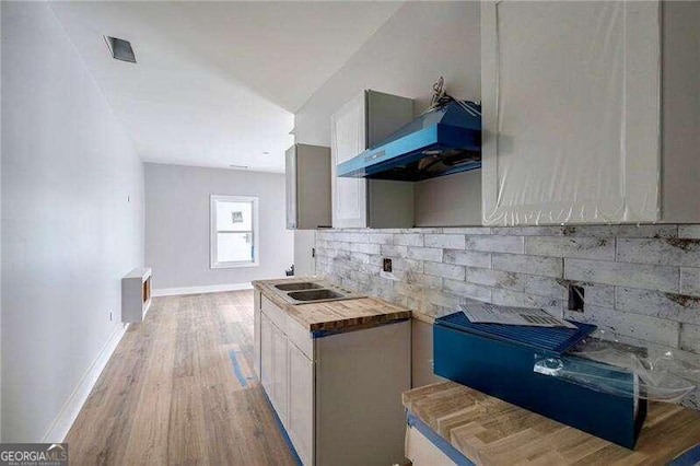 kitchen with butcher block counters, exhaust hood, light hardwood / wood-style floors, backsplash, and white cabinetry