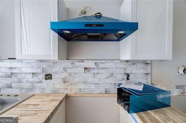 kitchen with white cabinets, tasteful backsplash, butcher block countertops, and exhaust hood