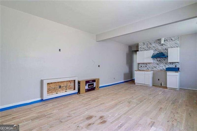 unfurnished living room with beamed ceiling and light hardwood / wood-style flooring