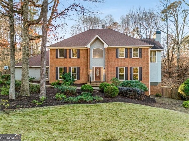 colonial house featuring a chimney, a front lawn, and brick siding