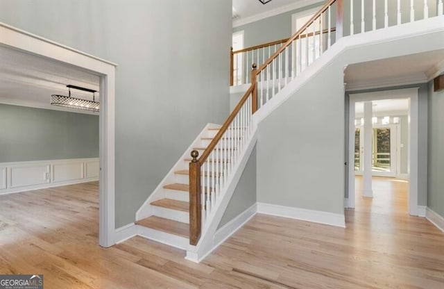 staircase with baseboards, crown molding, a high ceiling, and wood finished floors