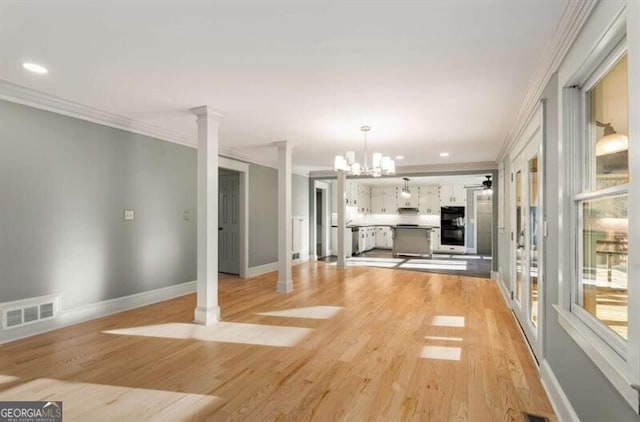 unfurnished living room featuring visible vents, light wood-style floors, baseboards, ornate columns, and crown molding