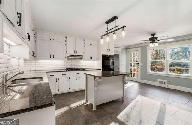 kitchen featuring dobule oven black, tasteful backsplash, under cabinet range hood, white cabinetry, and a sink