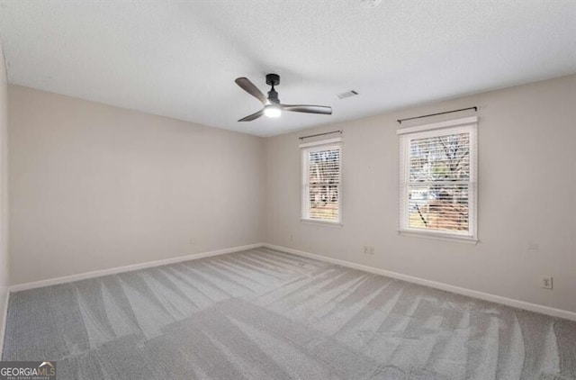 carpeted empty room featuring a textured ceiling, a ceiling fan, visible vents, and baseboards