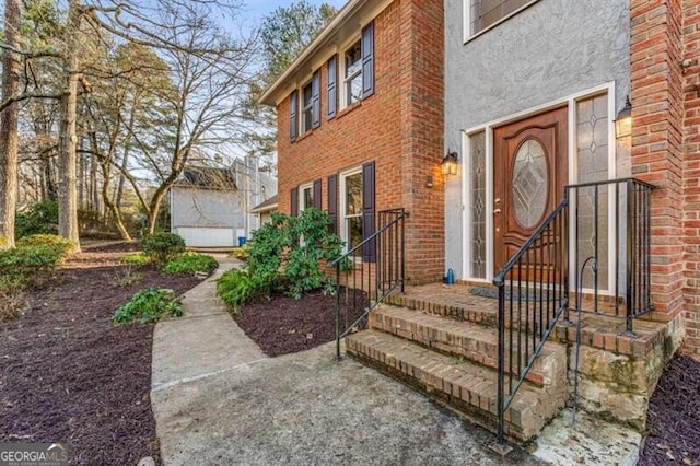 view of exterior entry with stucco siding and brick siding