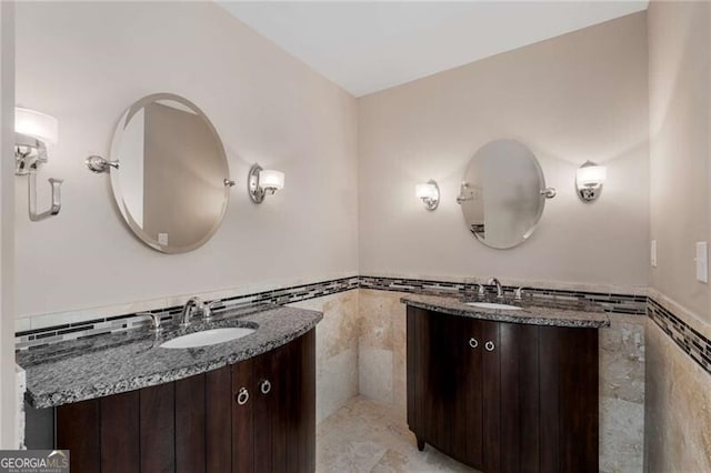 bathroom with wainscoting, two vanities, a sink, and tile walls