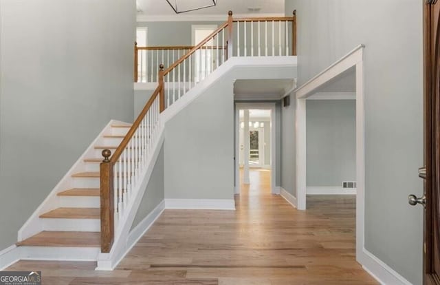 stairs with a high ceiling, wood finished floors, visible vents, and crown molding