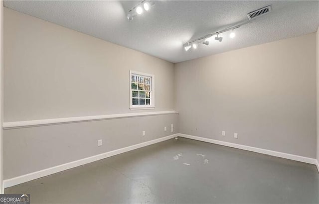 spare room featuring a textured ceiling, concrete floors, visible vents, and baseboards