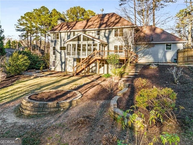 rear view of house featuring a sunroom, a chimney, stairway, fence, and a deck