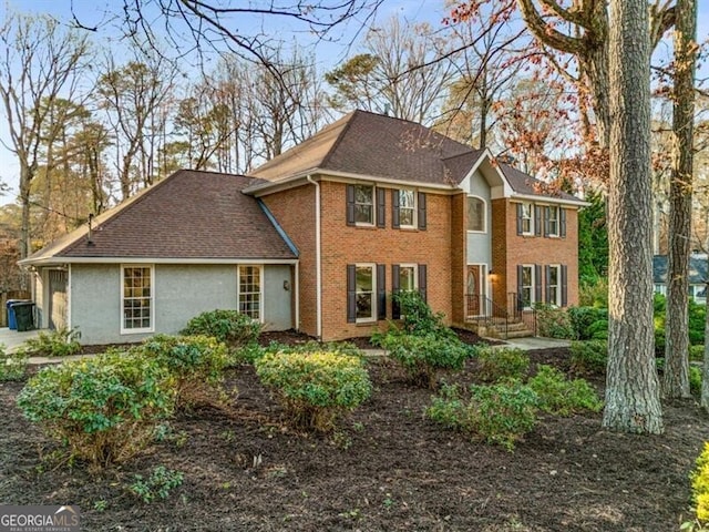 colonial inspired home featuring a shingled roof, a chimney, and brick siding