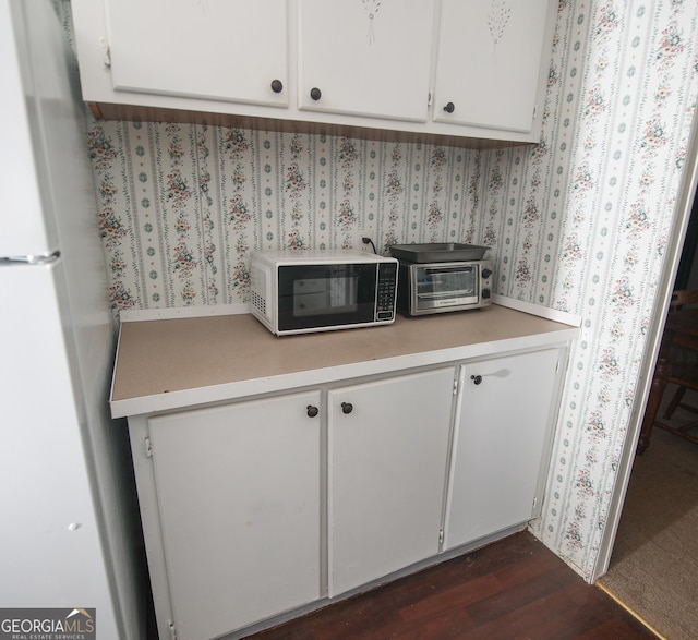 kitchen featuring a toaster, light countertops, freestanding refrigerator, and white cabinetry