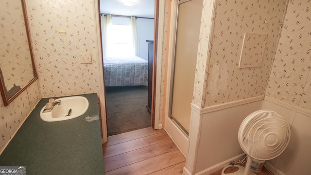 full bathroom featuring a stall shower, wallpapered walls, wood finished floors, and wainscoting