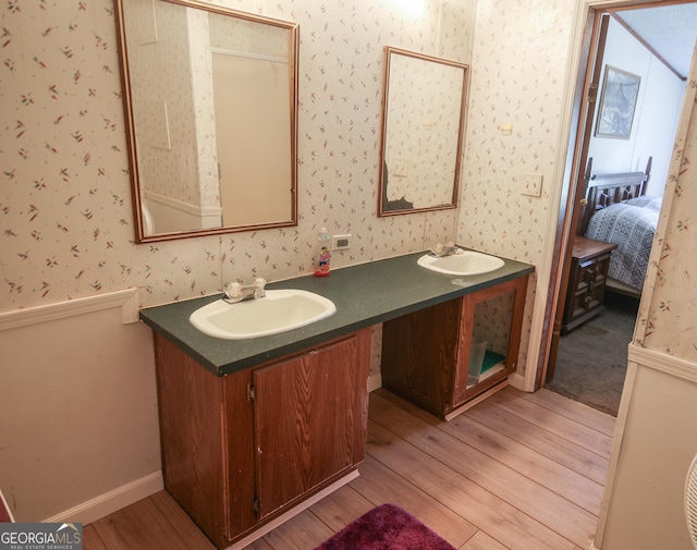 full bath with a sink, double vanity, wood finished floors, and wallpapered walls