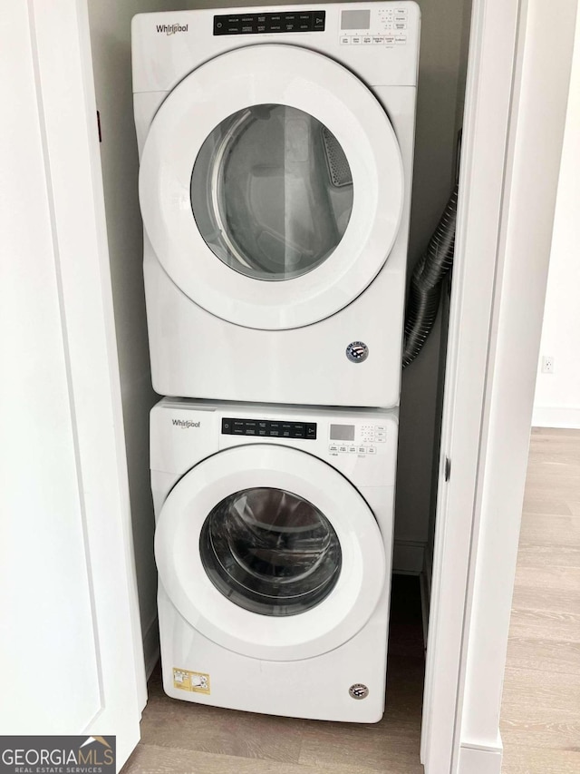 laundry area with stacked washer and clothes dryer and light hardwood / wood-style floors