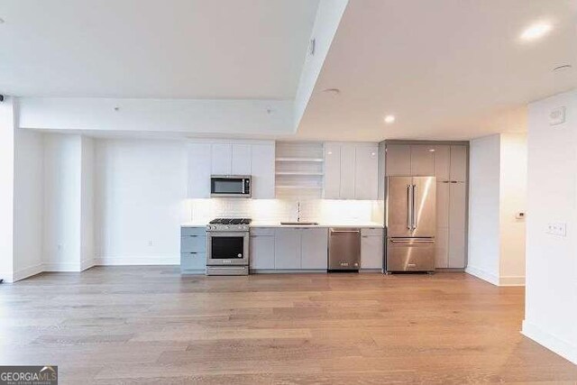 kitchen with gray cabinetry, stainless steel appliances, tasteful backsplash, and light hardwood / wood-style floors